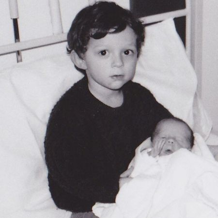 A young Tom Holland wearing a black sweater carrying his brother